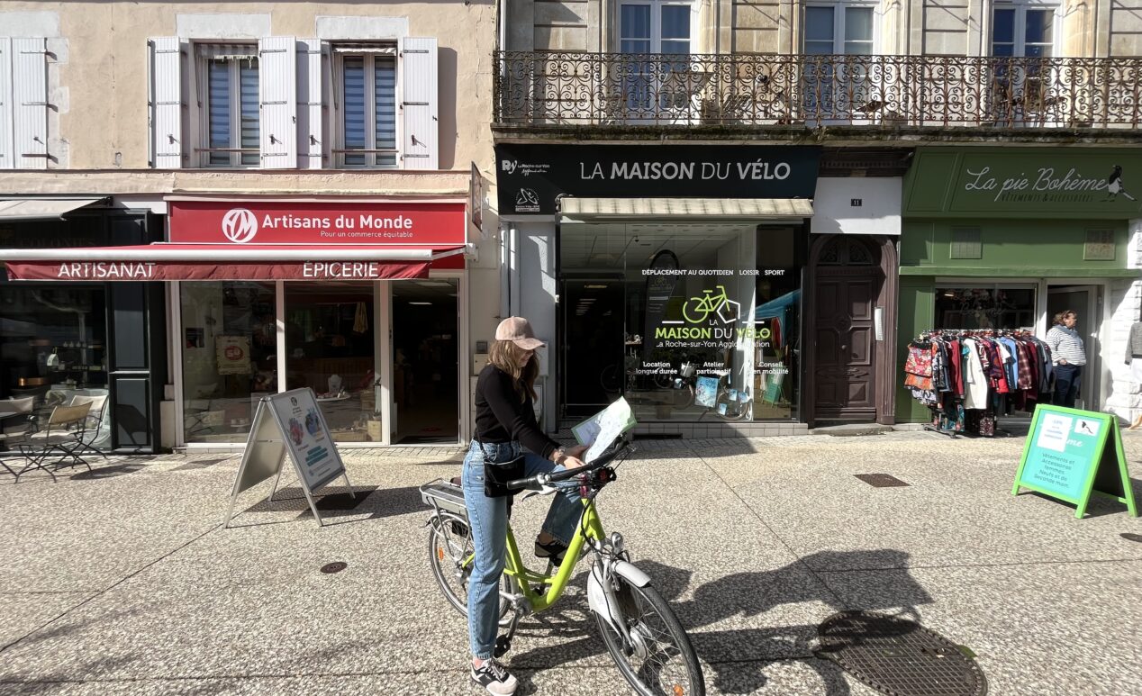Jeune cycliste devant la Maison du Vélo à La Roche-sur-Yon qui tient dans ses mains la carte des aménagements cyclables